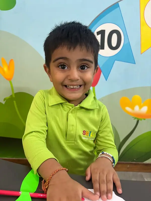 A boy in a green Skill-ed T-shirt beams from his craft table