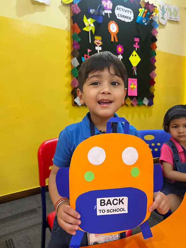 A smiling boy holding up his Back to School backpack craft