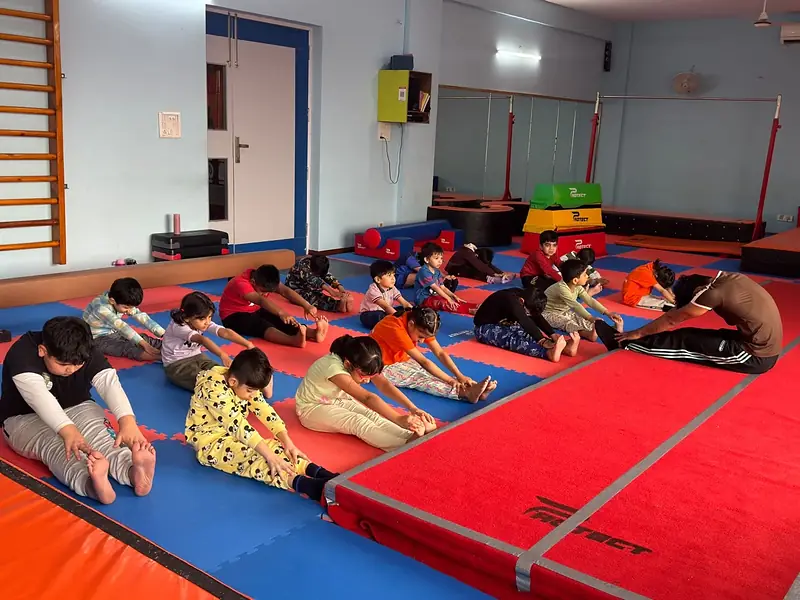 Children stretch on the mats with their coach in a gymnastics class